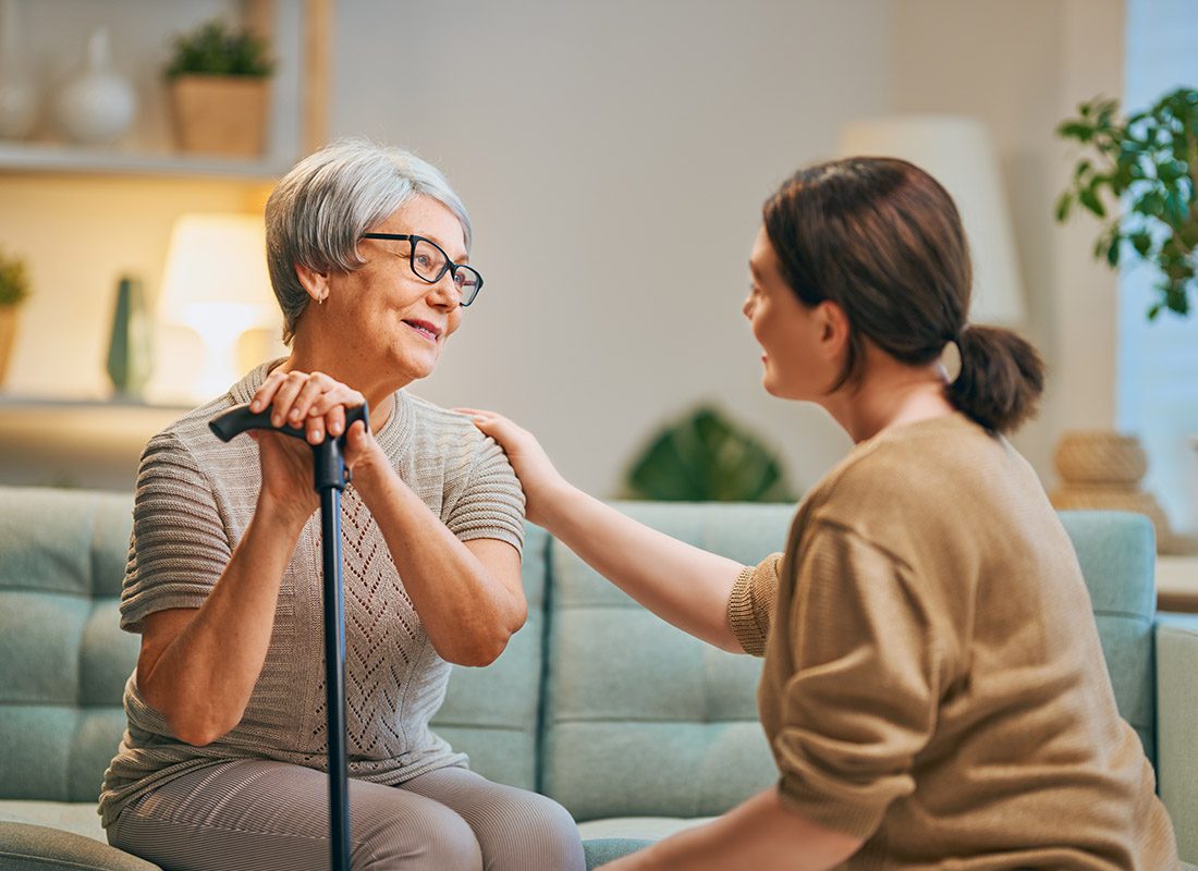 Home Health Care Insurance - Nurse Talking with Older Woman with Cane While Sitting in the Older Womans Living Room at Home